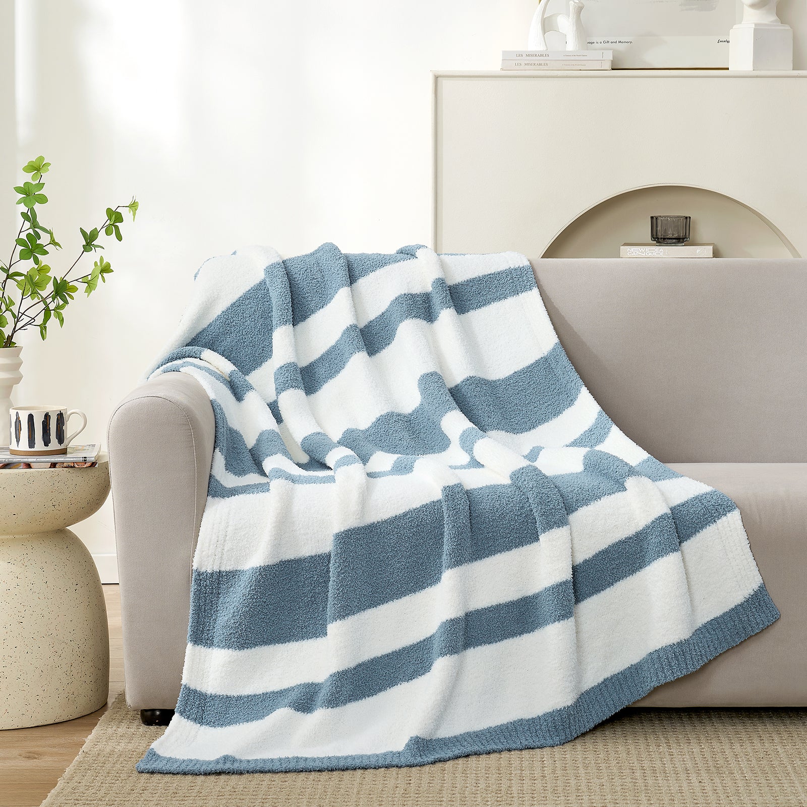Snuggle Sacs Reversible Blue Striped Feather Yarn Knit Throw Blanket draped on a grey couch with mug and plant behind#color_Blue