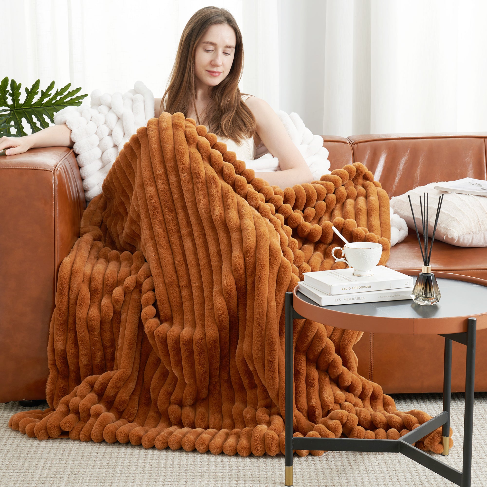 Woman relaxing on sofa with a striped faux fur throw blanket in Burnt Orange while reading #color_Burnt Orange
