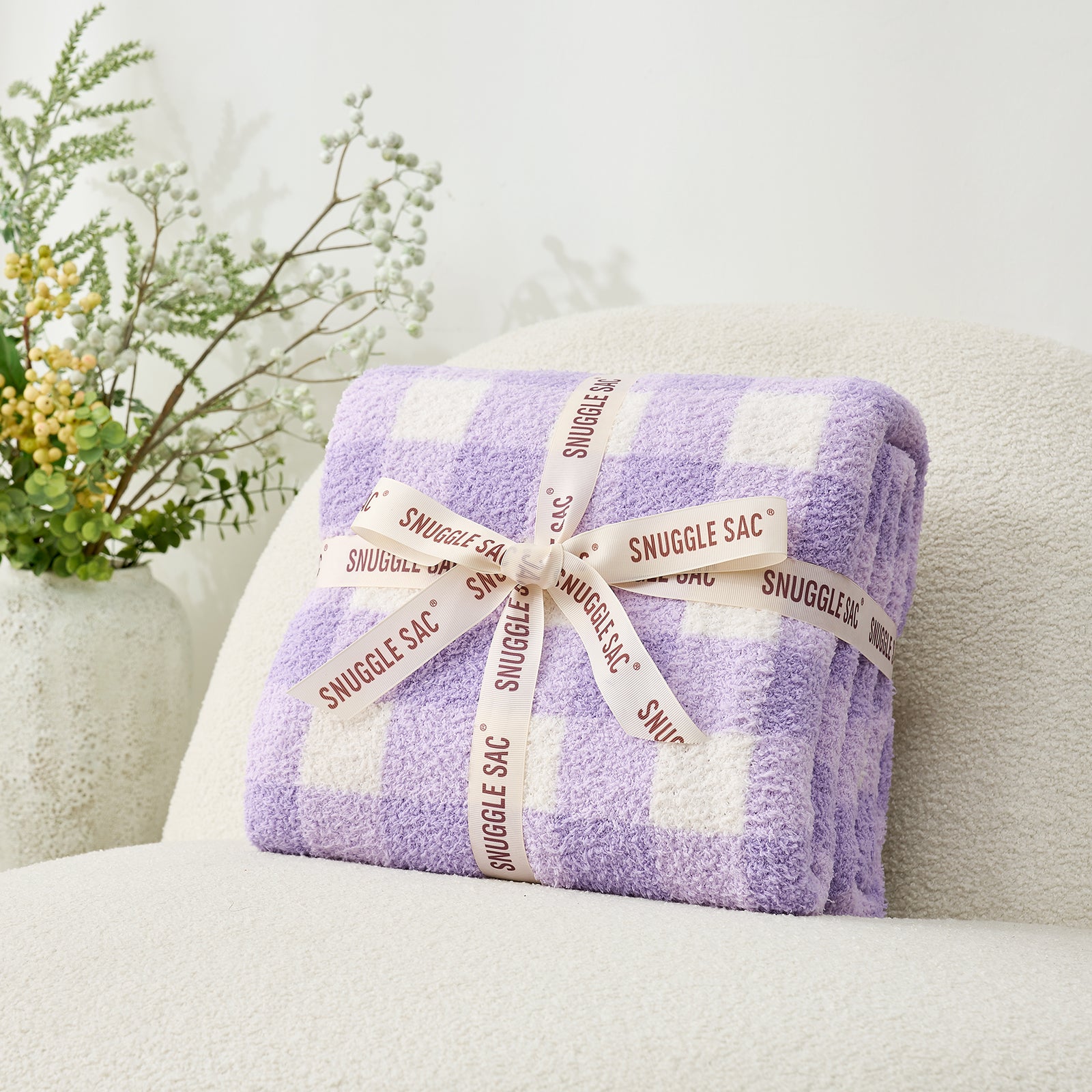 Plaid-patterned Snuggle Sac wrapped with a ribbon on a gray chair. #color_Purple