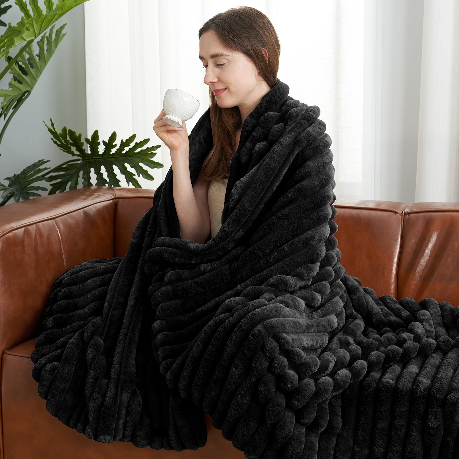 Woman relaxing on sofa with a striped faux fur throw blanket in Black while holding a cup #color_Black
