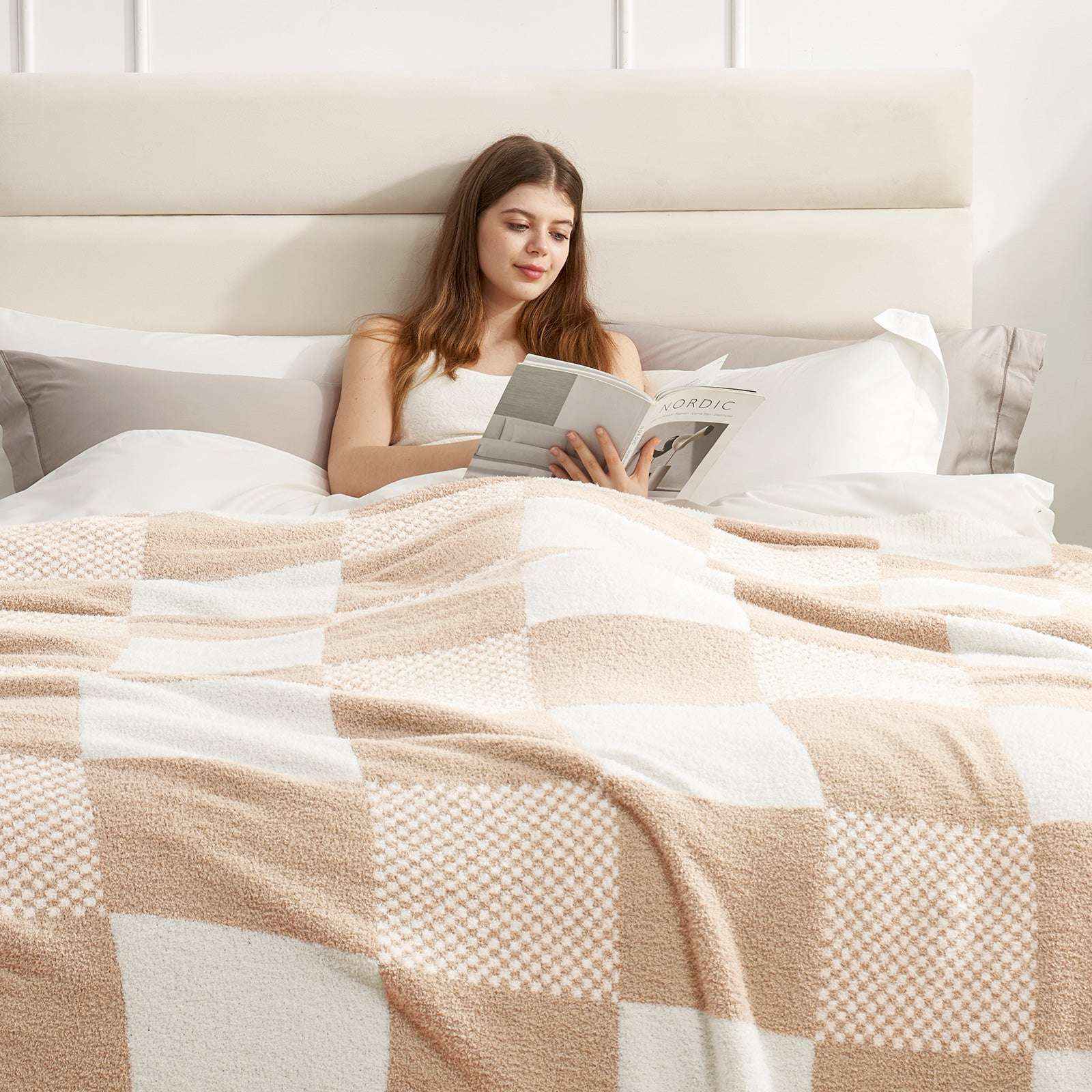 A woman laying on bed reading a book with Snuggle Sac Checkered Feather Yarn Knit Throw Blanket on her#Color_Beige