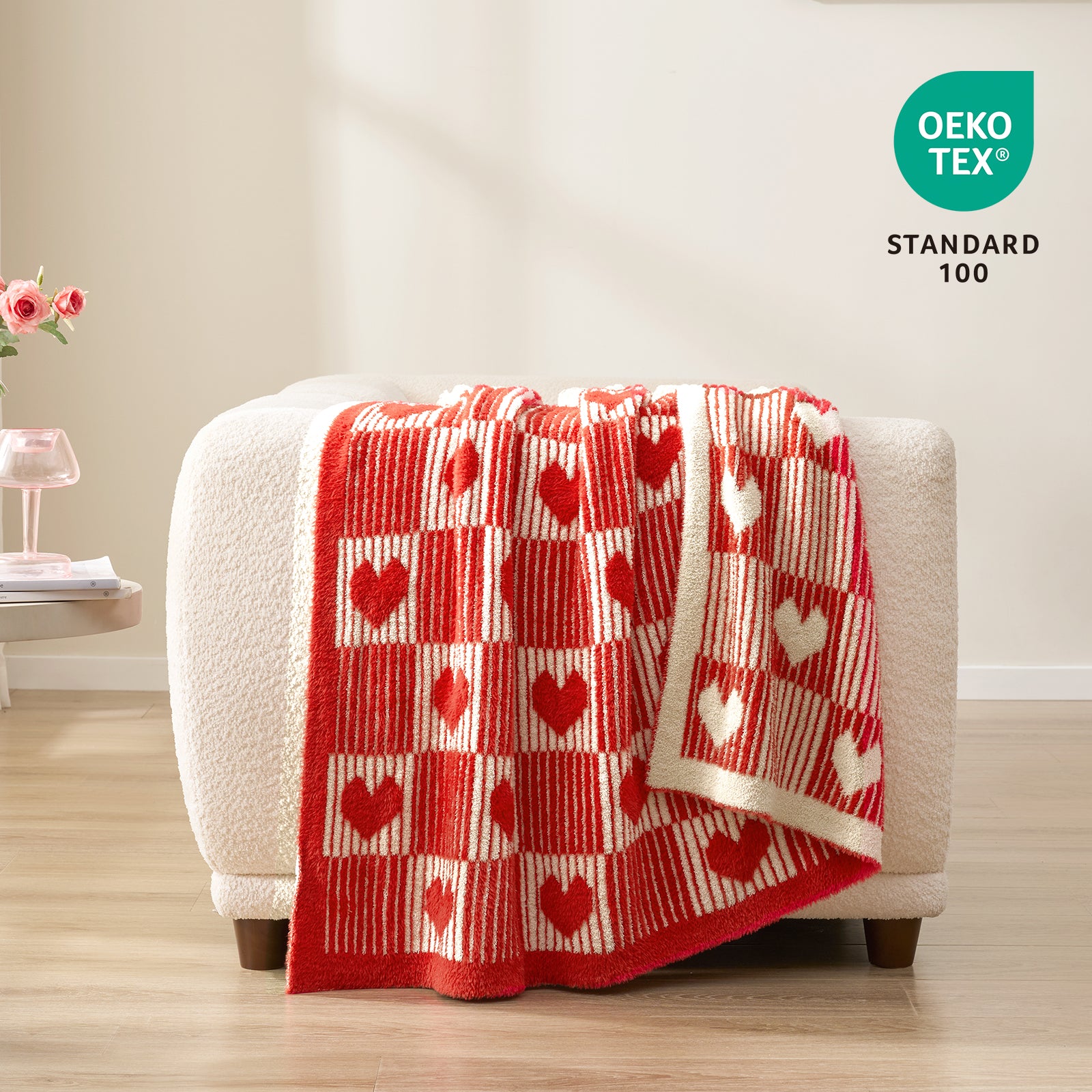 Red and white checkered blanket with heart patterns draped over a white chair, featuring OEKO-TEX Standard 100 logo. #color_Red/Cream
