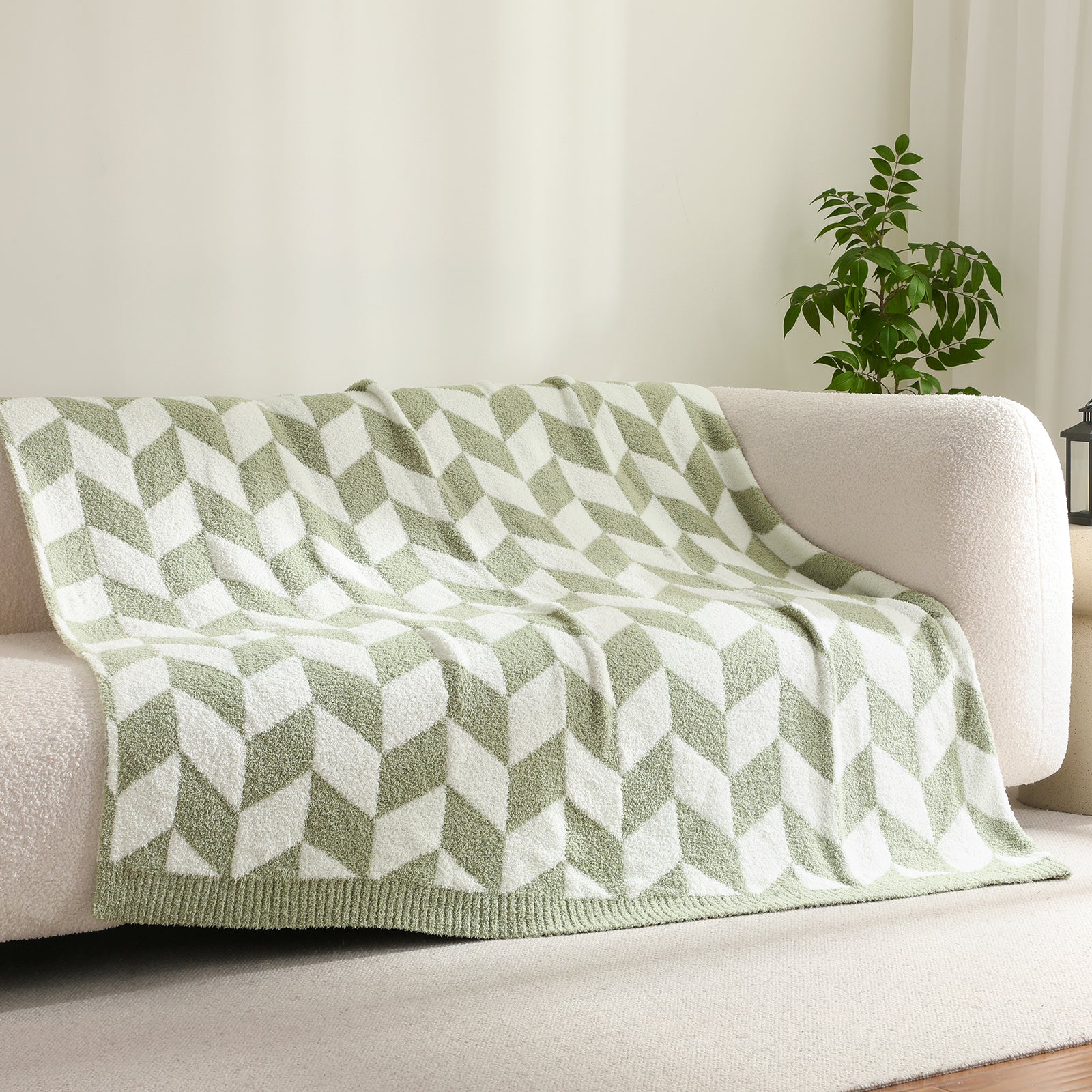 Folded Snuggle Sacs Chevron Feather Yarn Knit Throw Blanket on the couch with plant next to it#color_Sage Green