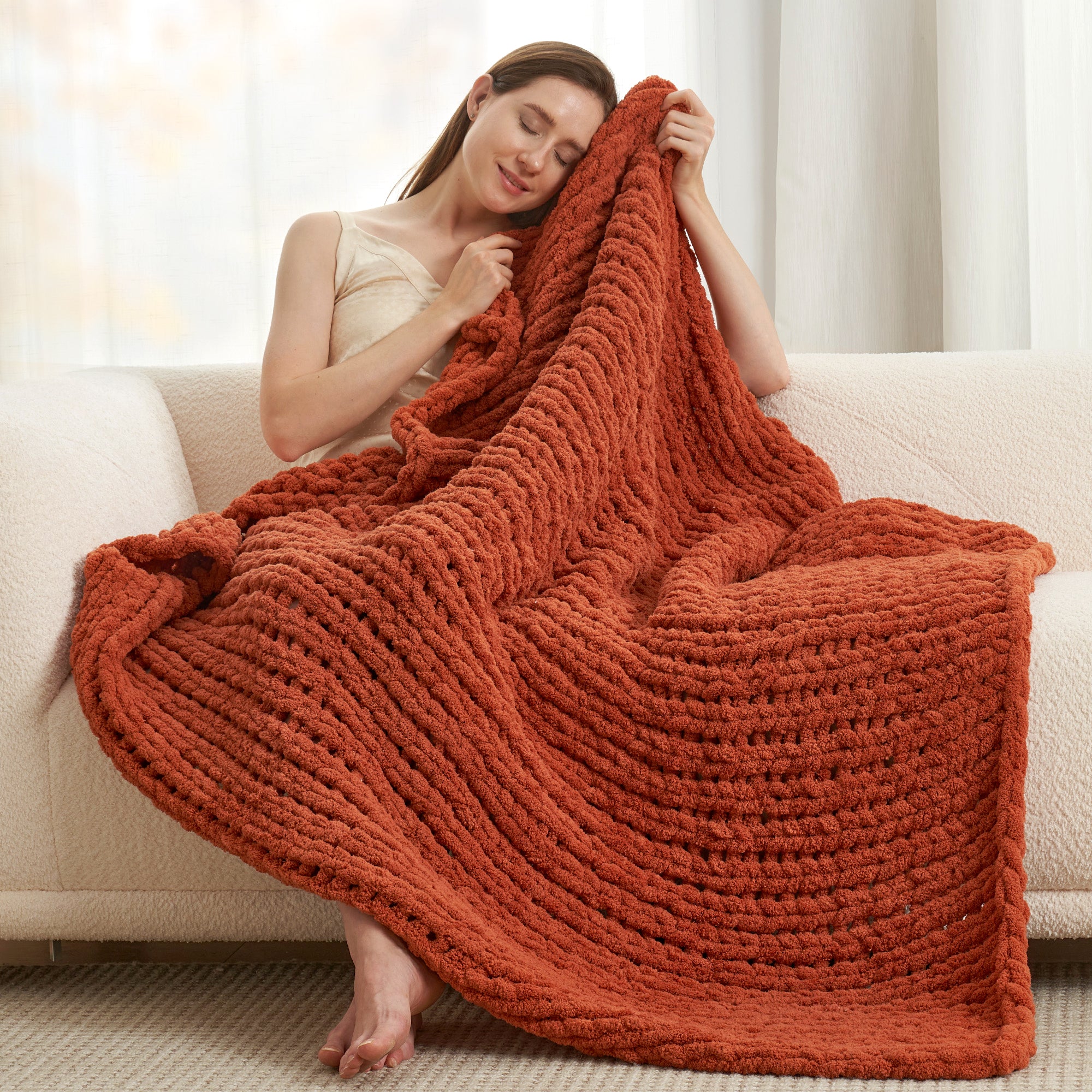 Woman relaxing on sofa wrapped in a chunky knit throw blanket in Burnt Orange #color_Burnt Orange