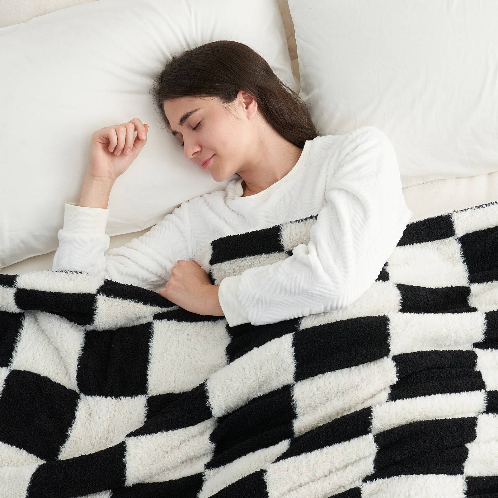 A woman laying down on the bed under UltraCozy Checkered Feather Yarn Knit Throw Blanket#Color_Black White