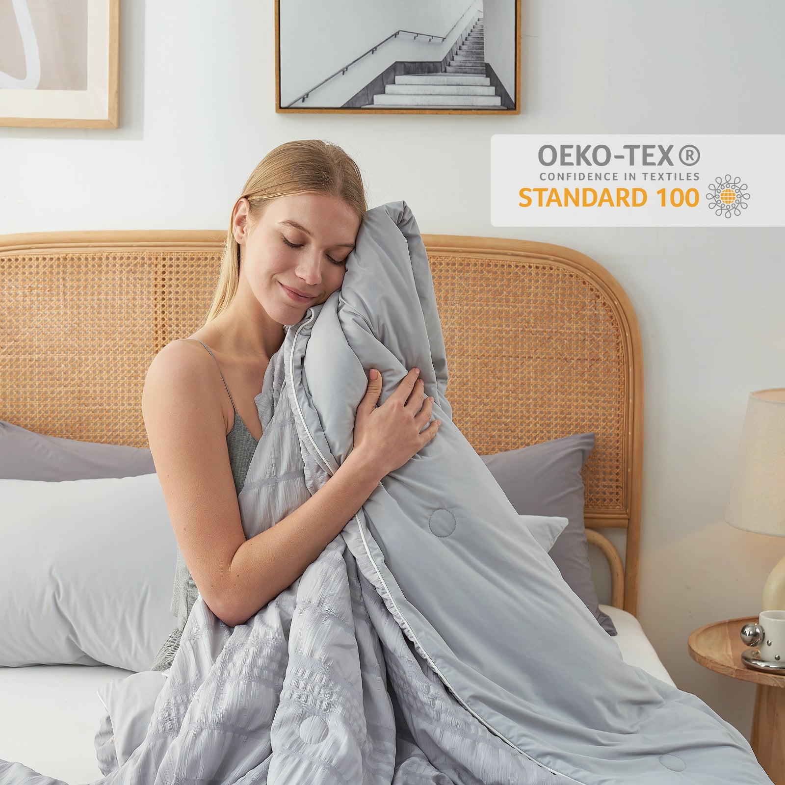 A woman touching her face with Snuggle Sac Cooling comforter sitting on the bed proving OEK0-TEX certificate#color_Light Grey