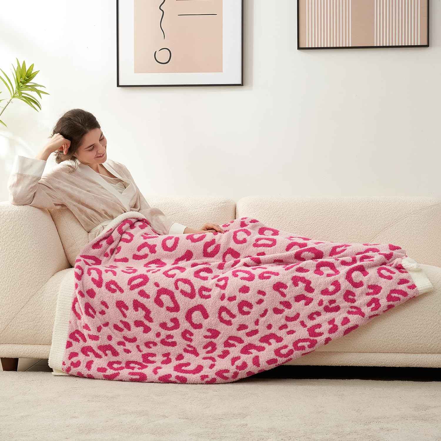 A woman laying on a beige couch wrapped in Reversible Leopard Feather Yarn Knit Throw Blanket #Color_Hot Pink