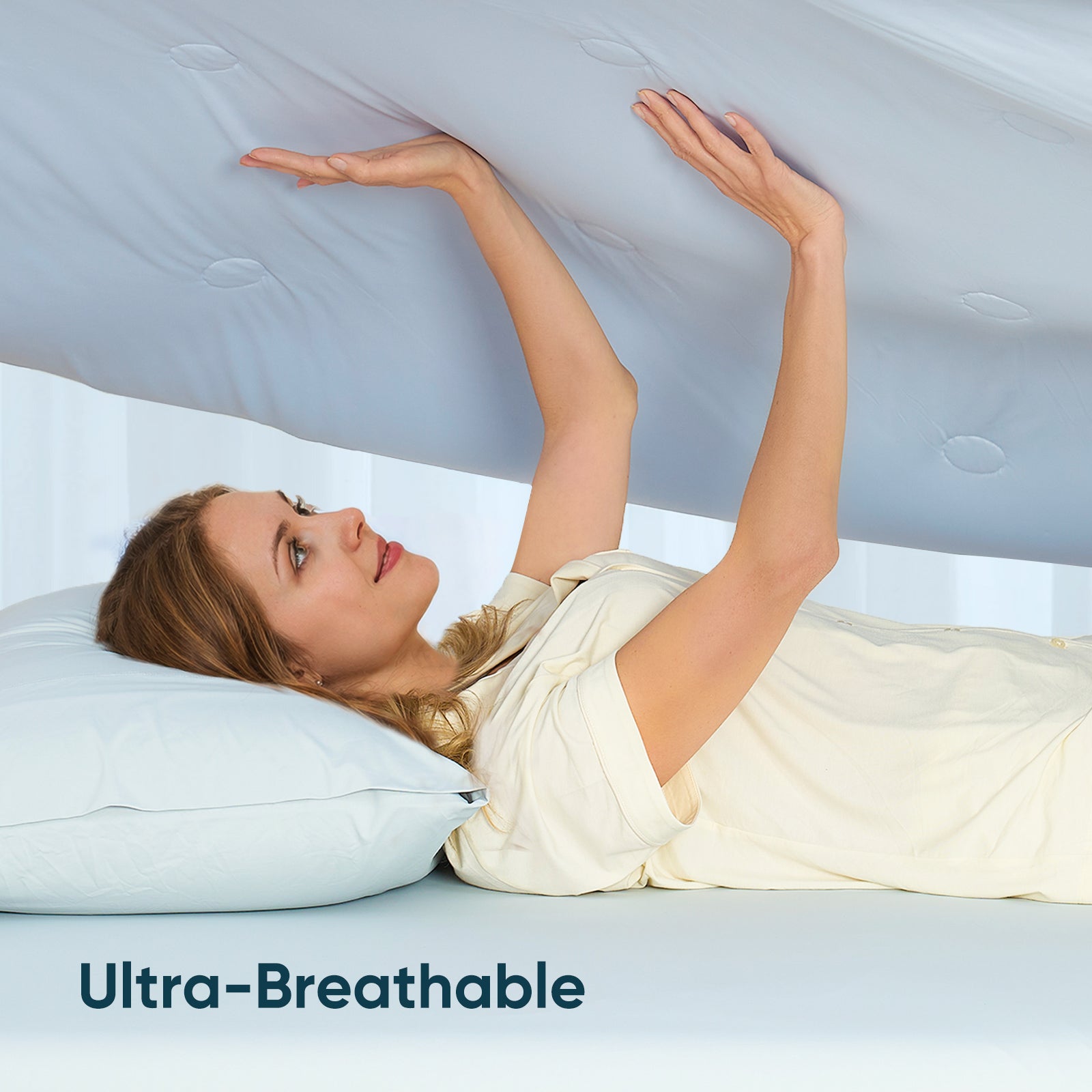A woman laying down on the bed holding on Snuggle Sac Cooling comforter showing ultra breathable #color_Blue