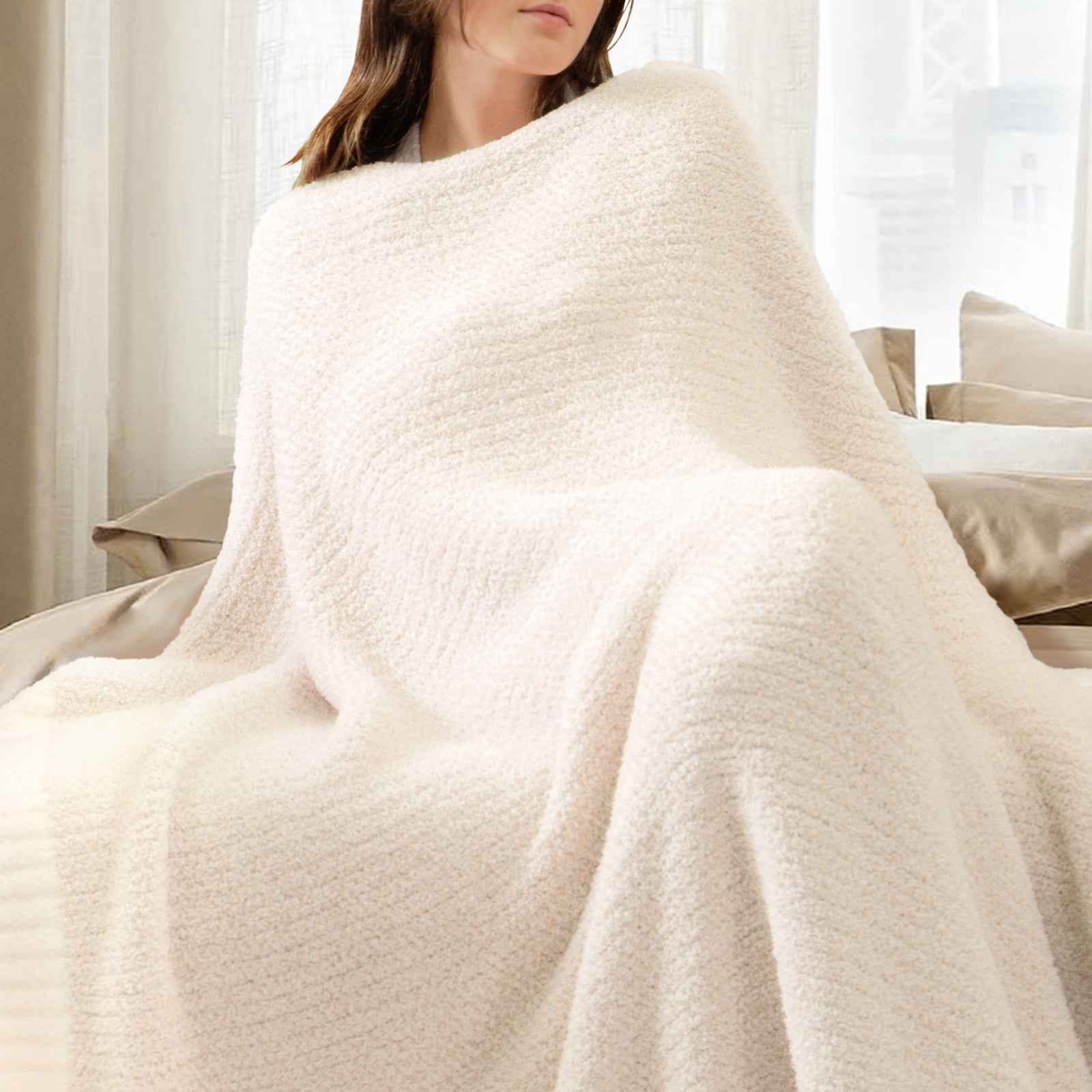 A woman wrapped in Snuggle Sac Heather Feather Yarn Ivory Knit Throw Blanket #Color_Ivory
