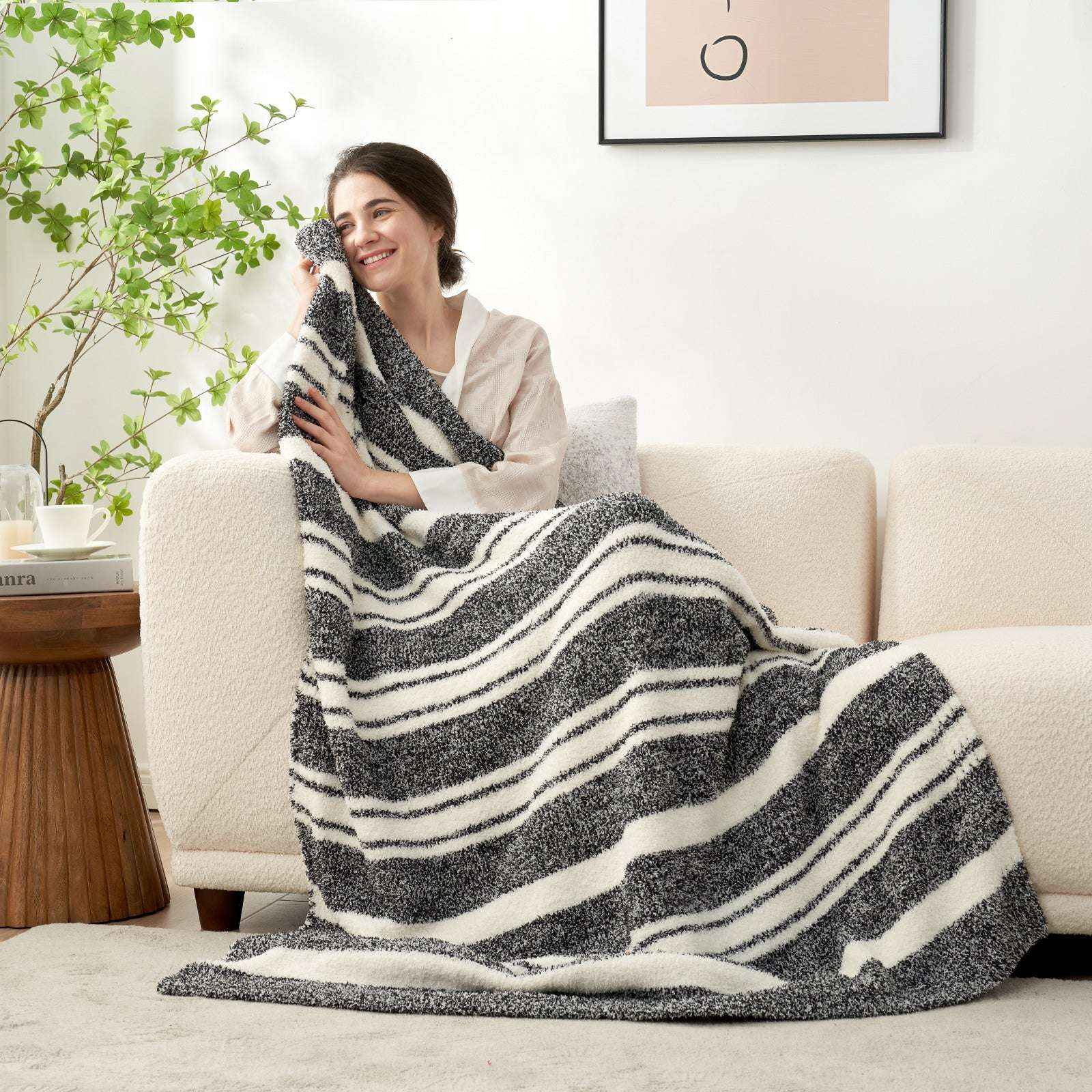 A woman wrapped in Striped Feather Yarn Knit Throw Blanket on a beige couch#Color_Black