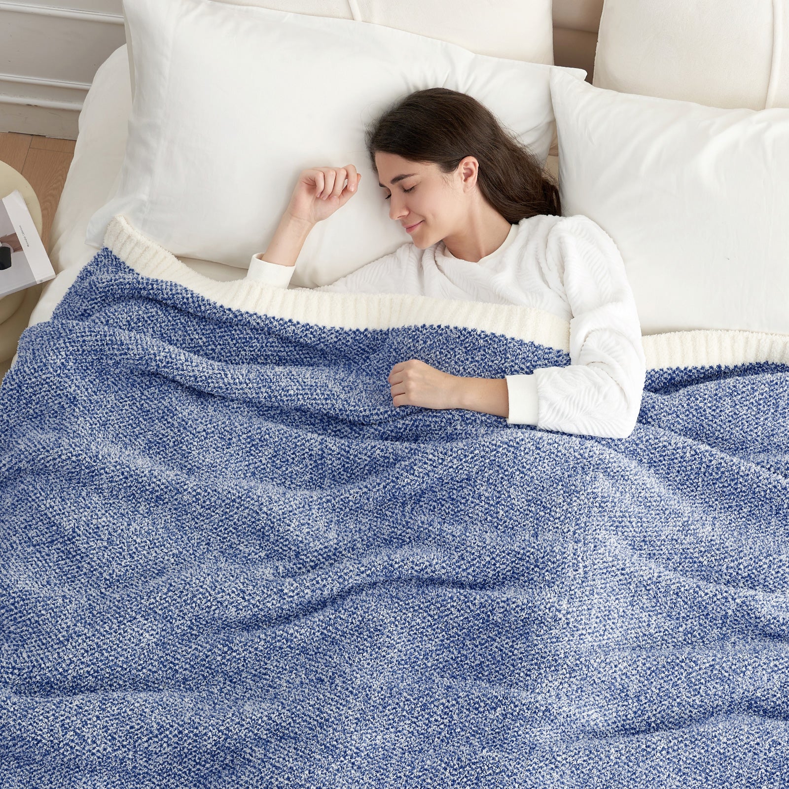 A woman laying on the bed with Snuggle Sac Heather Feather Yarn heather  Royal blue Knit Throw Blanket #color_Heather Royal Blue