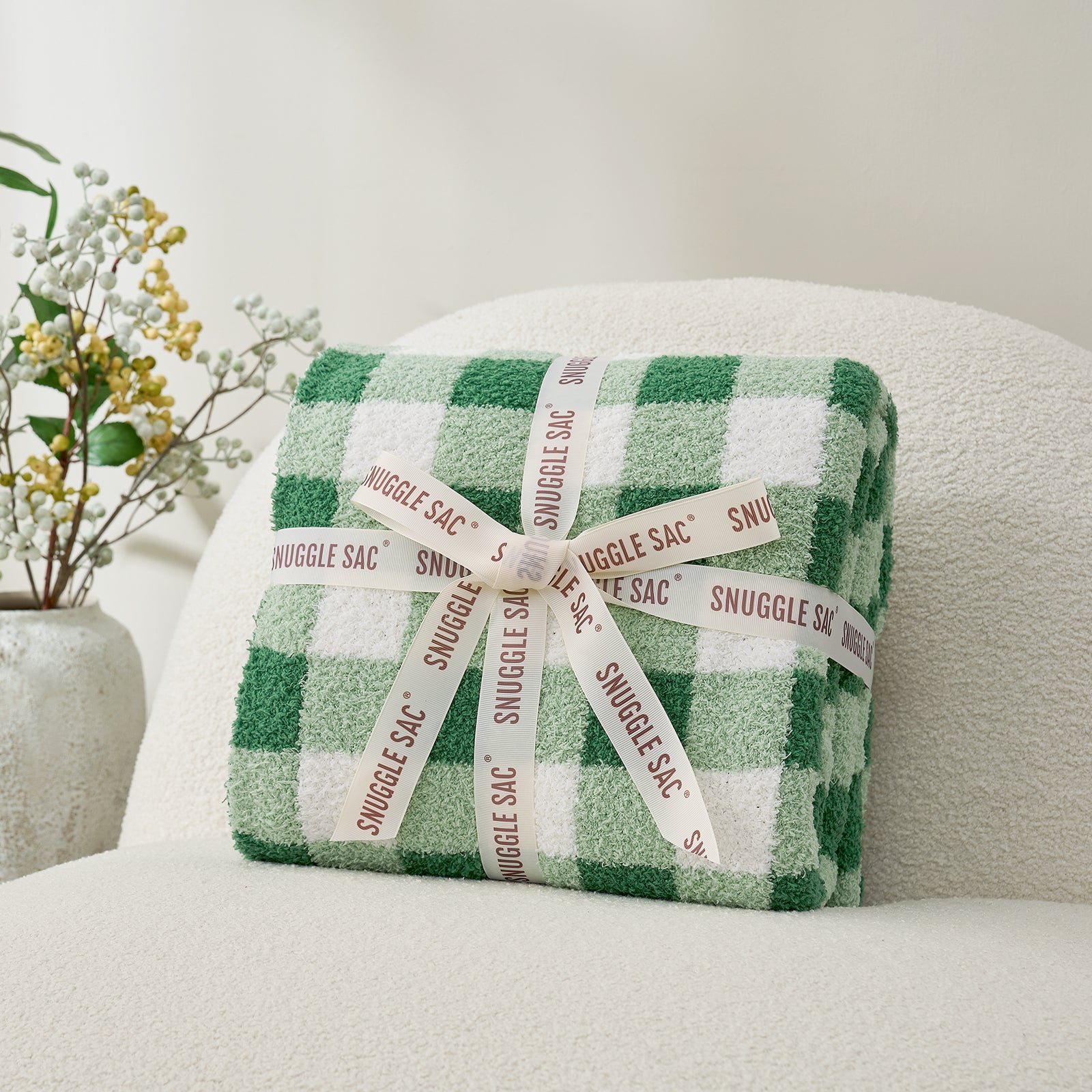 Plaid-patterned Snuggle Sac wrapped with a ribbon on a gray  chair. #color_Green