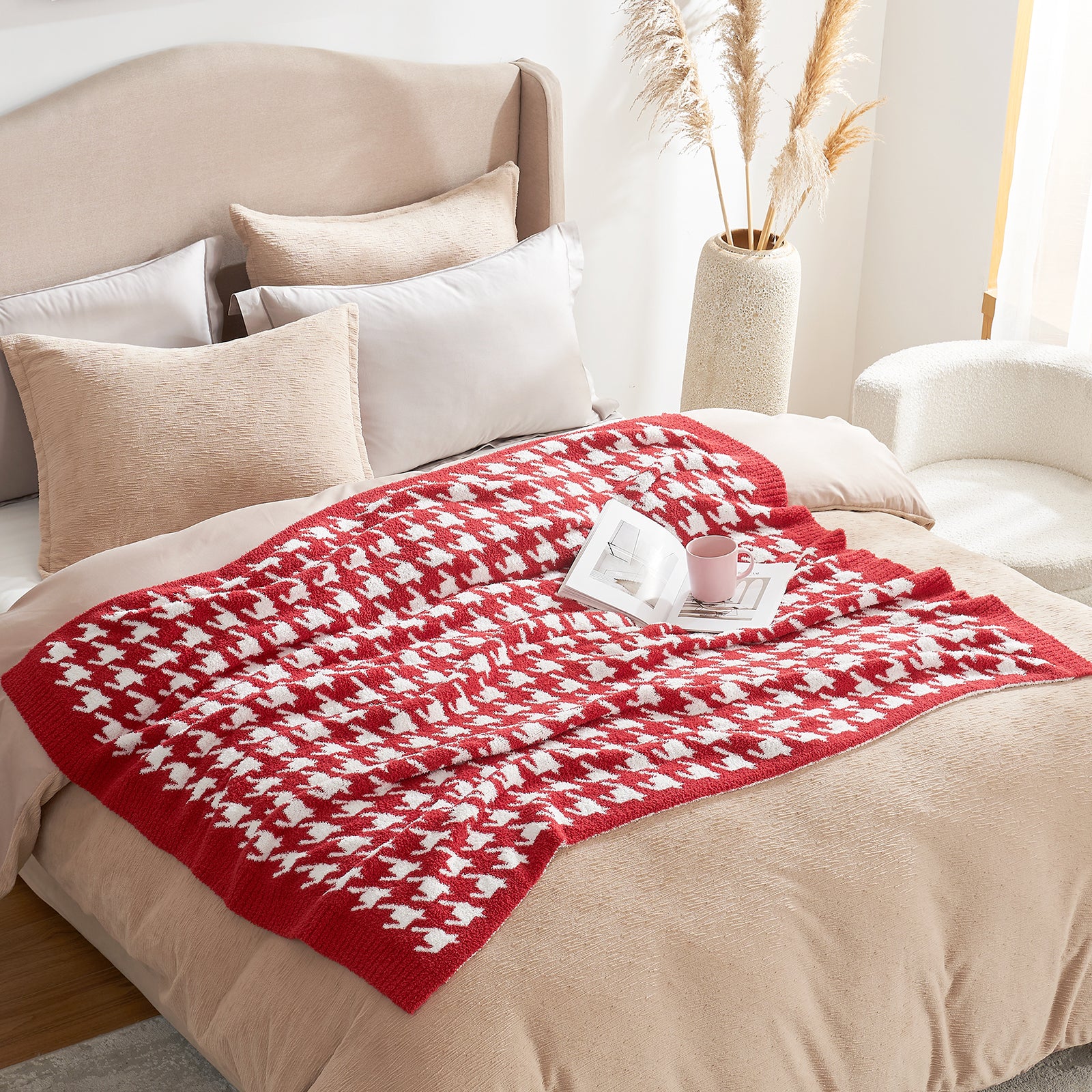 Red and white patterned blanket on a bed with pillows and a cup in a cozy room.  #Color_Red/Cream
