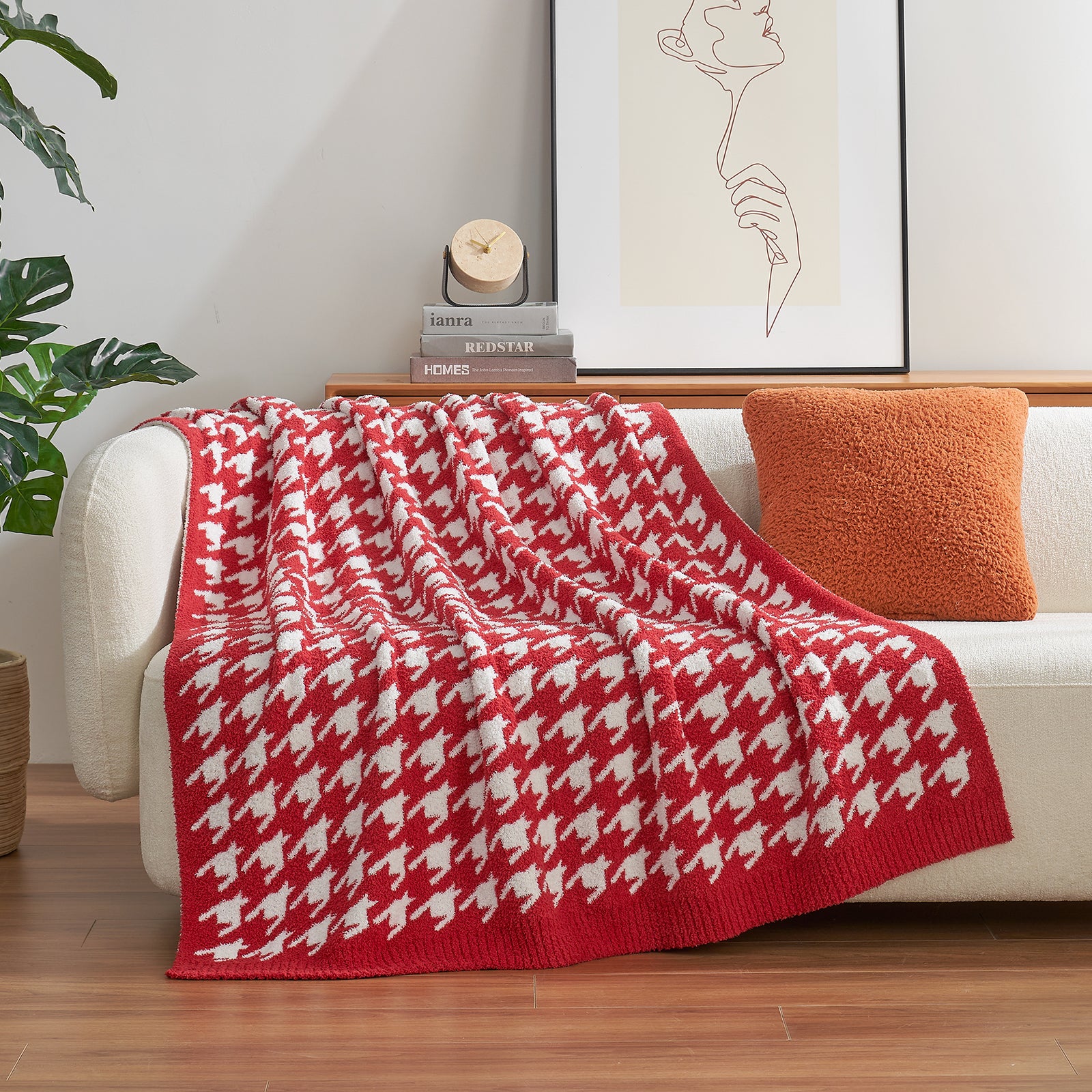 Red and white patterned blanket draped over a white sofa with an orange pillow, in a living room setting.  #Color_Red/Cream