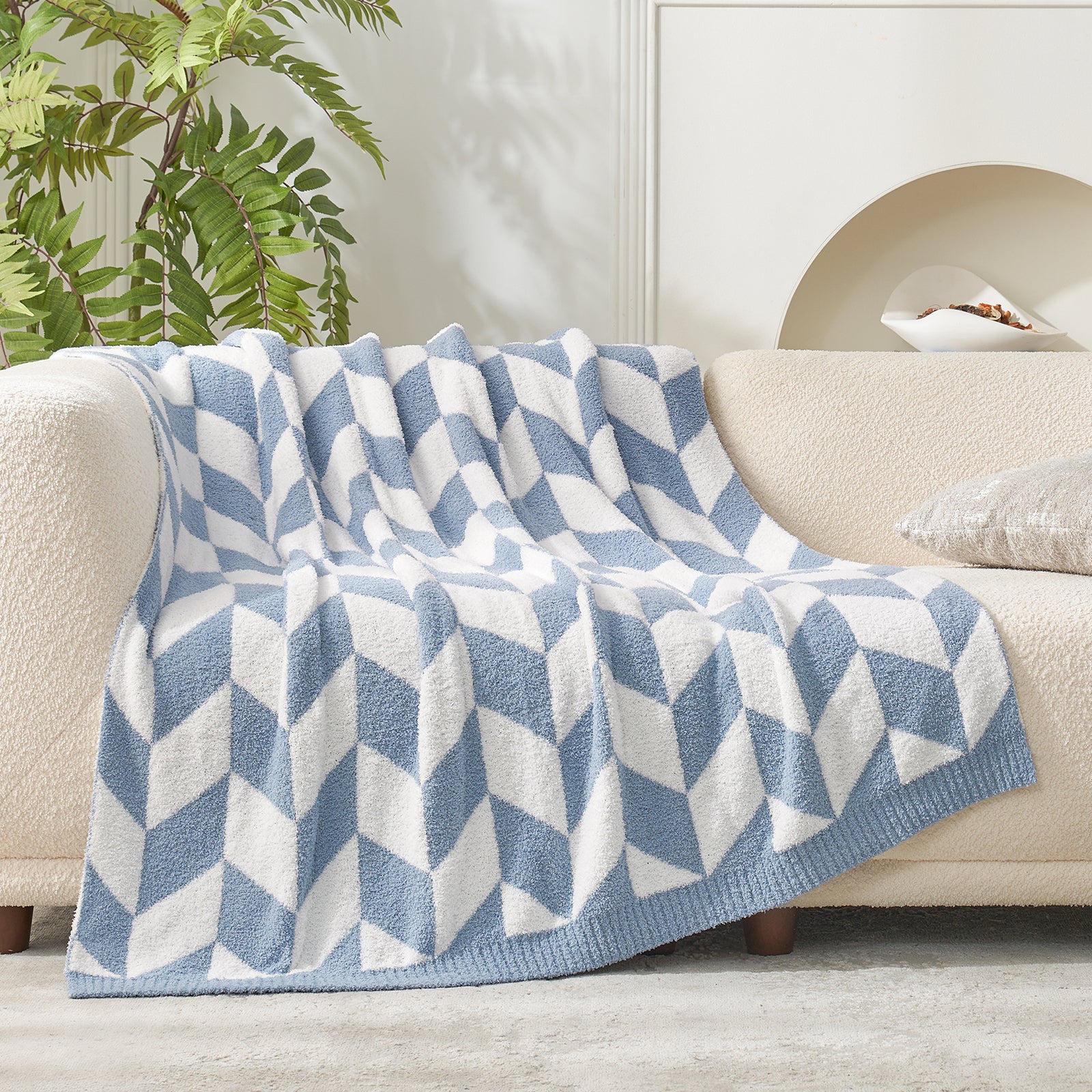 Folded Snuggle Sacs Chevron Feather Yarn Knit Throw Blanket on the couch with plant next to it#color_Blue