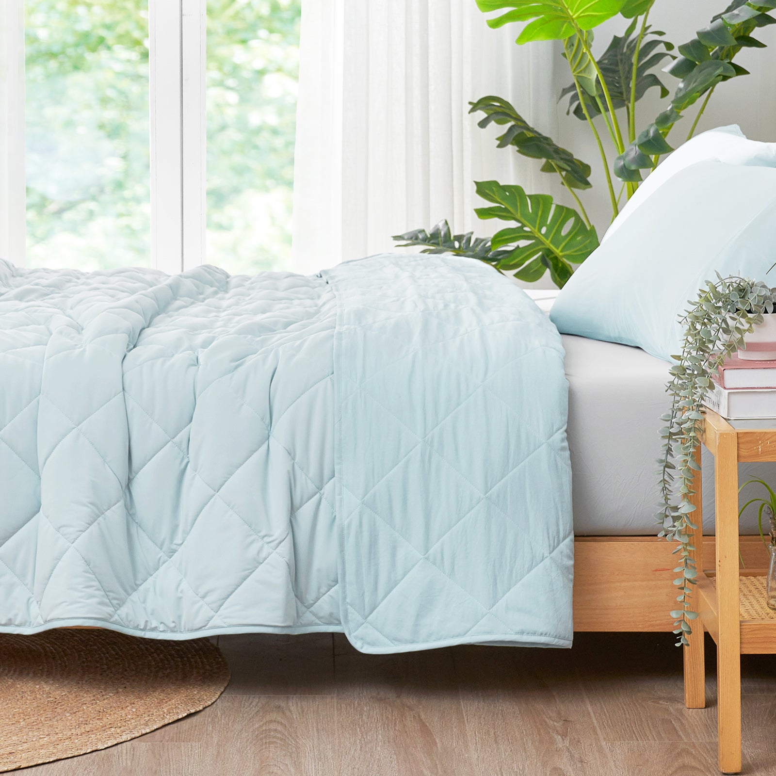 Right side view of ced with a Snuggle Sac blue cooling comforter in a bright room with plants.#color_Blue