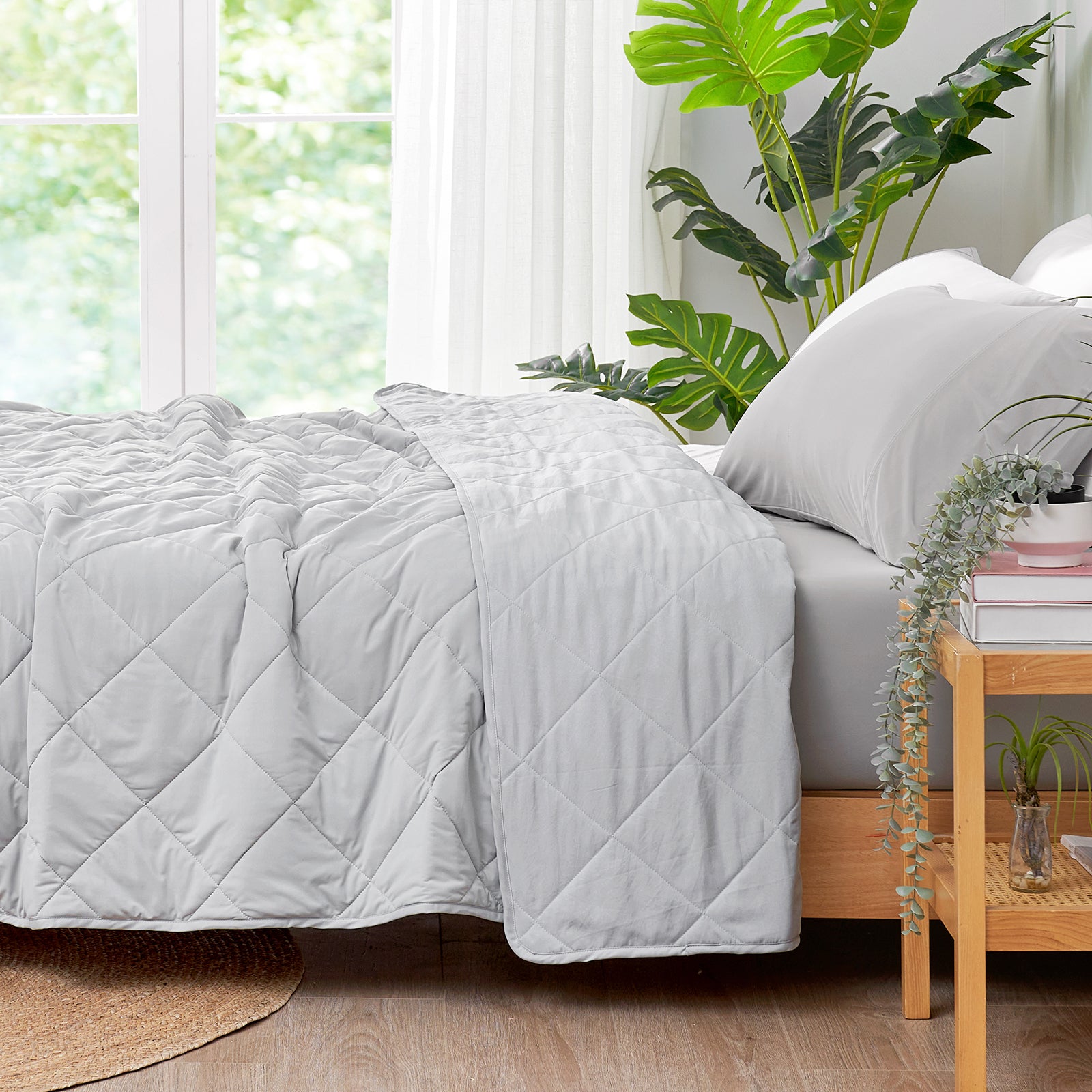 Right side view of ced with a Snuggle Sac grey cooling comforter in a bright room with plants.#color_Light Grey