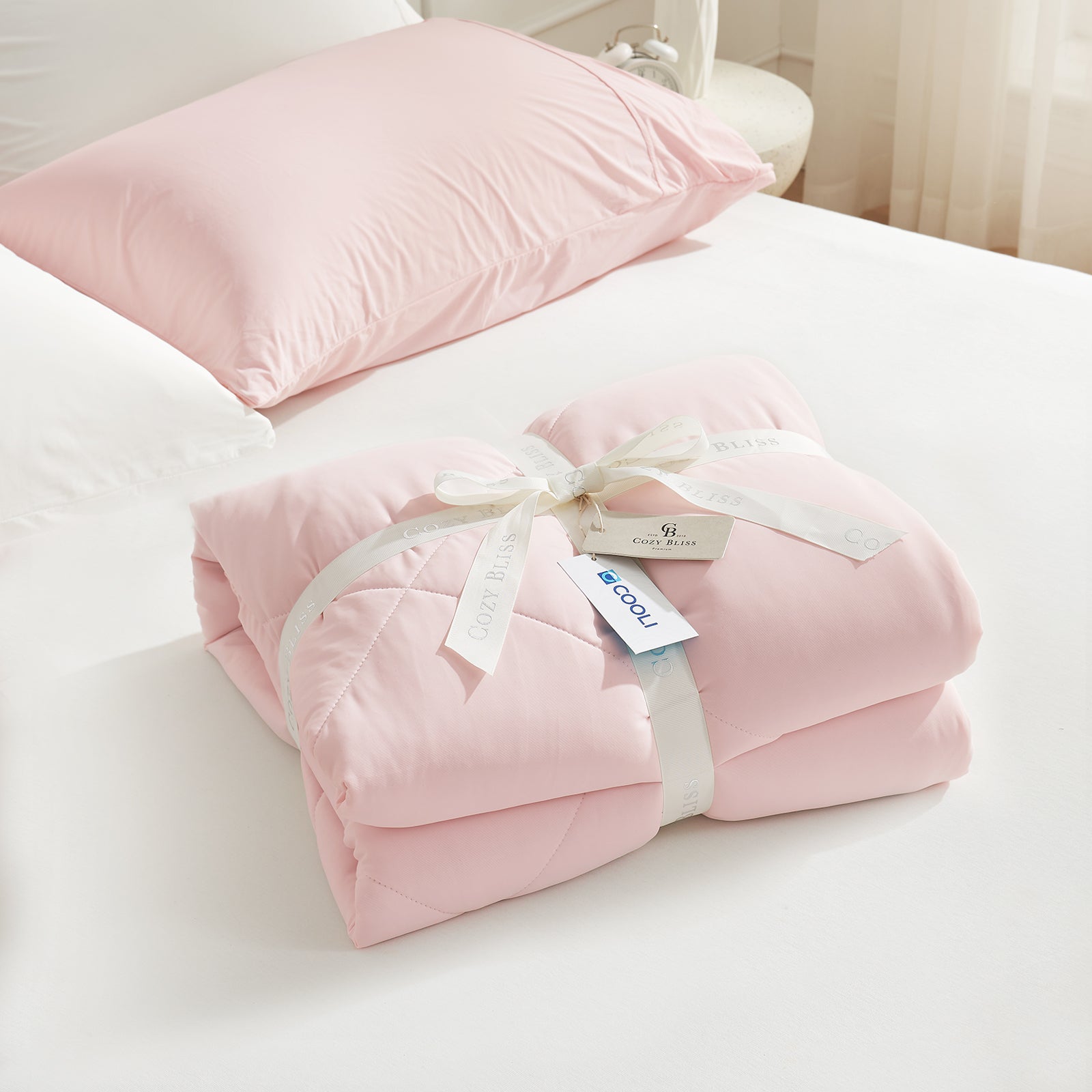 Pink/Grey Snuggle Sac Cooling comforter with a white ribbon on bed, perfect as gift.#color_Pink/Grey