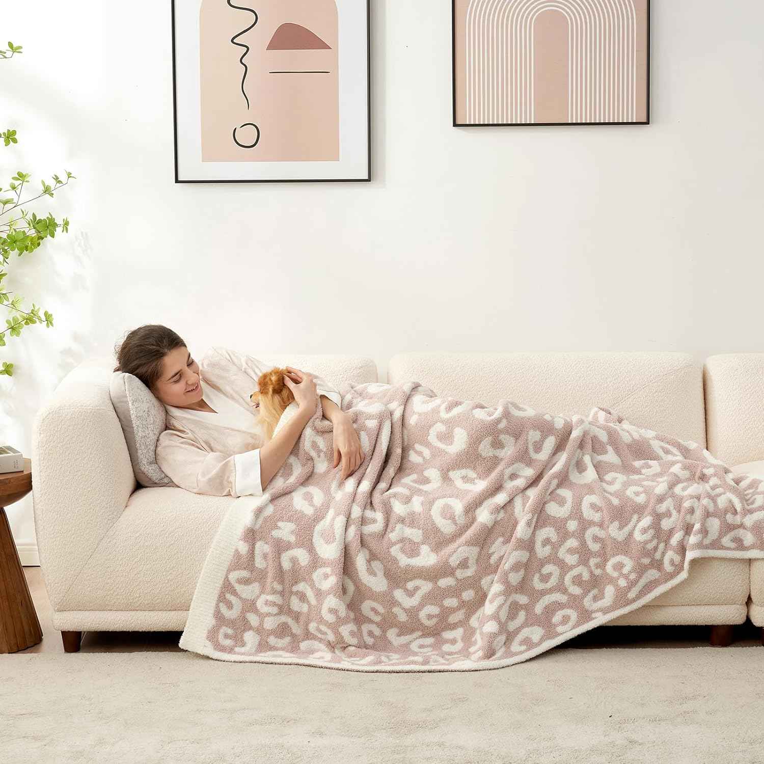 A woman laying on a beige couch wrapped in Reversible Leopard Feather Yarn Knit Throw Blanket with a dog #Color_Leopard Beige