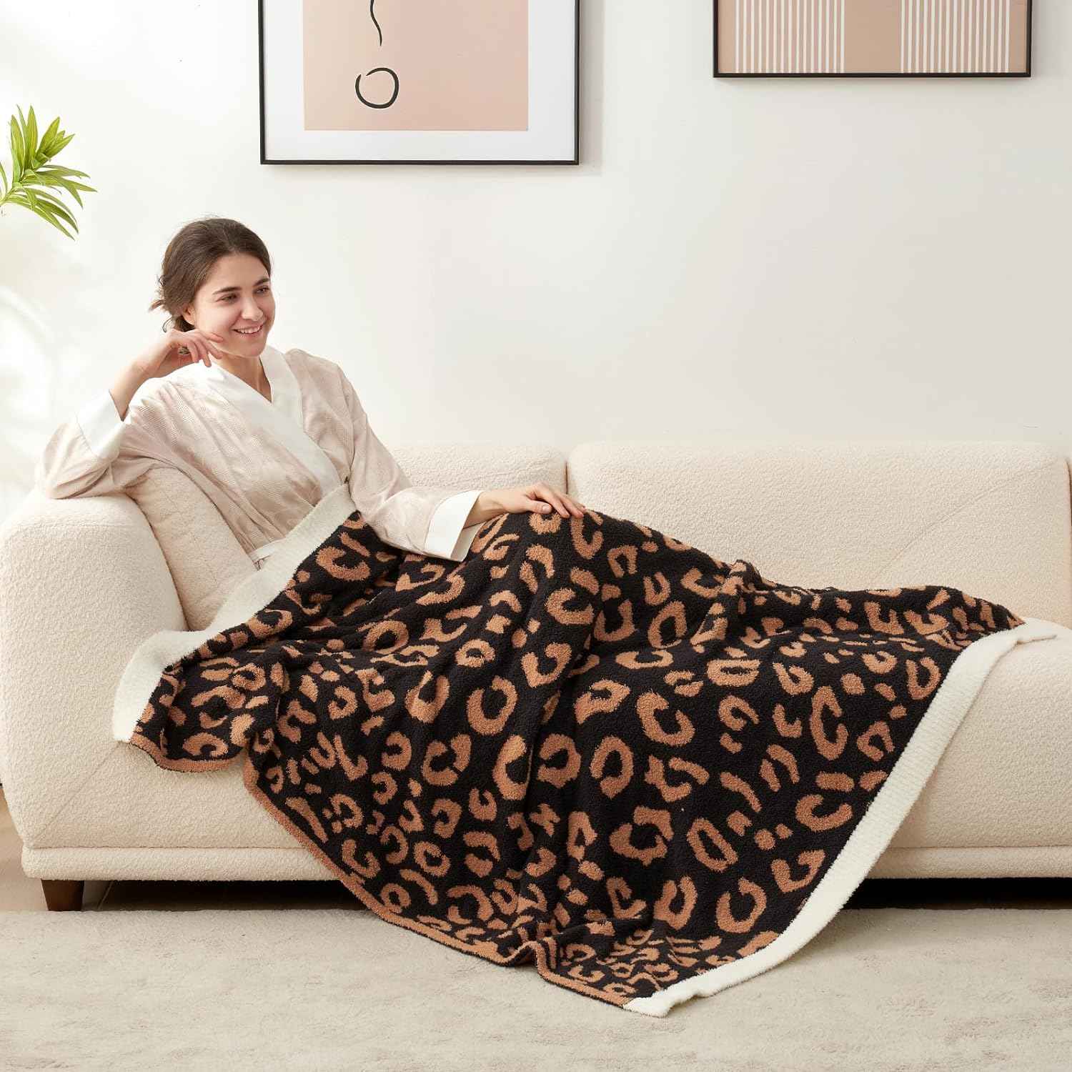 A woman laying on a beige couch wrapped in Reversible Leopard Feather Yarn Knit Throw Blanket #Color_Black