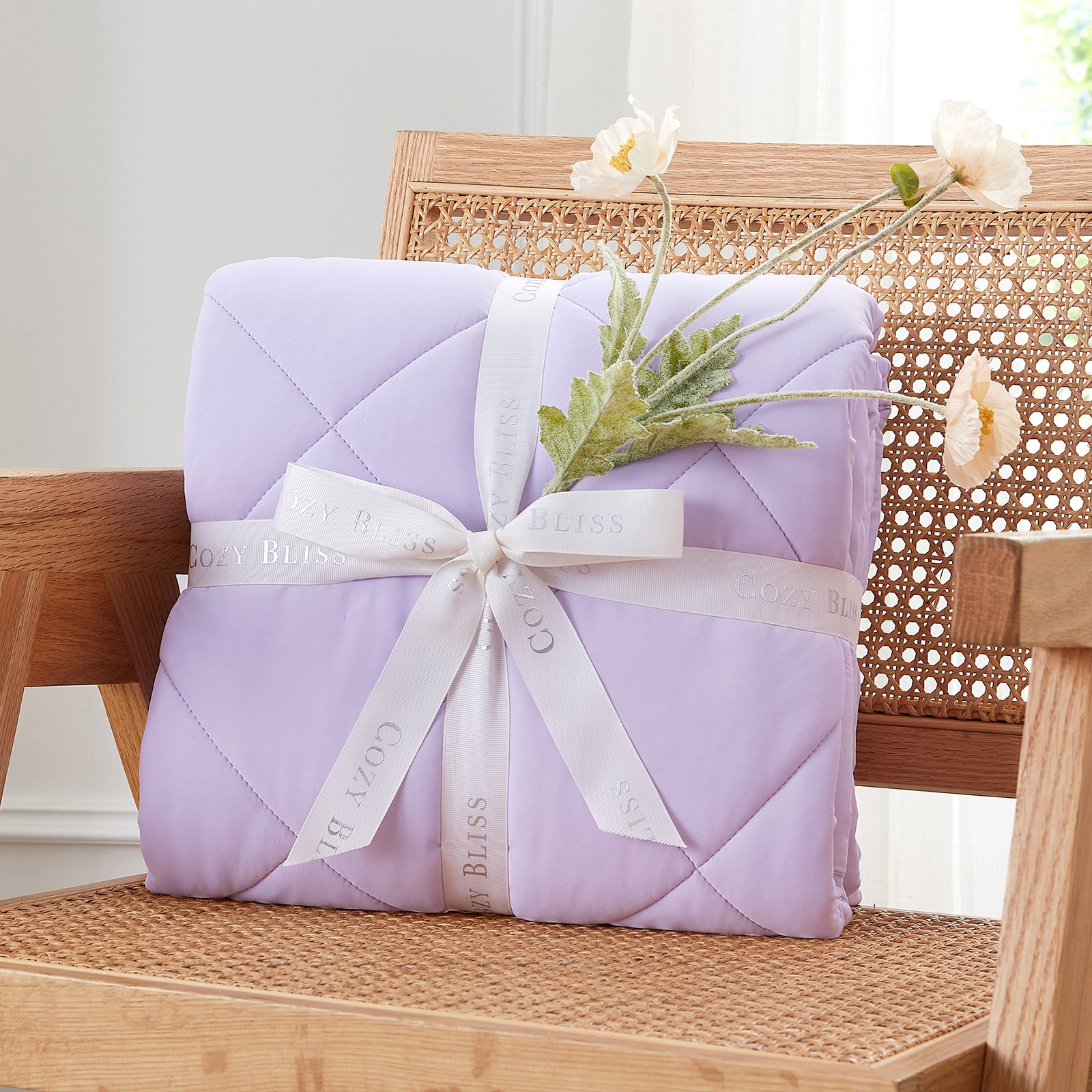 Folded Snuggle Sac purple comforter with white ribbon on chair surrounded by plants, presented as a perfect gift#color_Purple