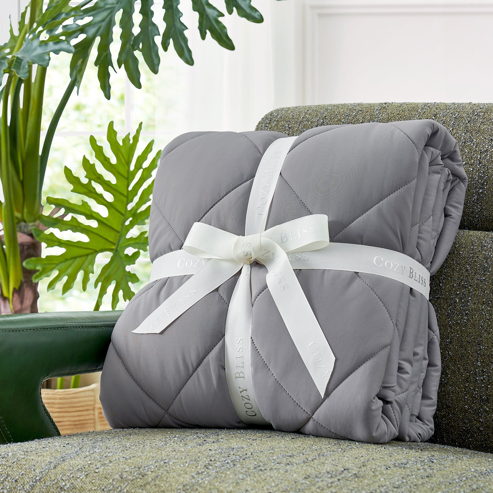 Folded comforter with white ribbon on green couch surrounded by plants, presented as a perfect gift#color_Dark Grey