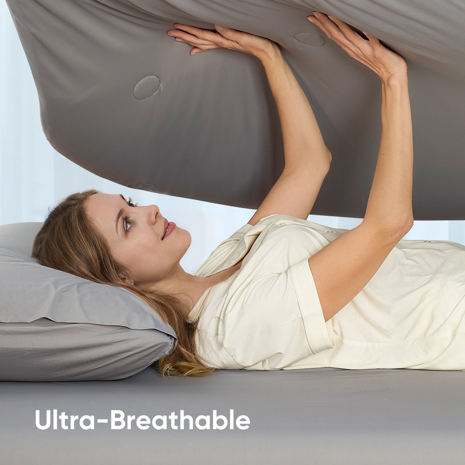 A woman laying down on the bed holding on Snuggle Sac Cooling comforter showing ultra breathable#color_Dark Grey