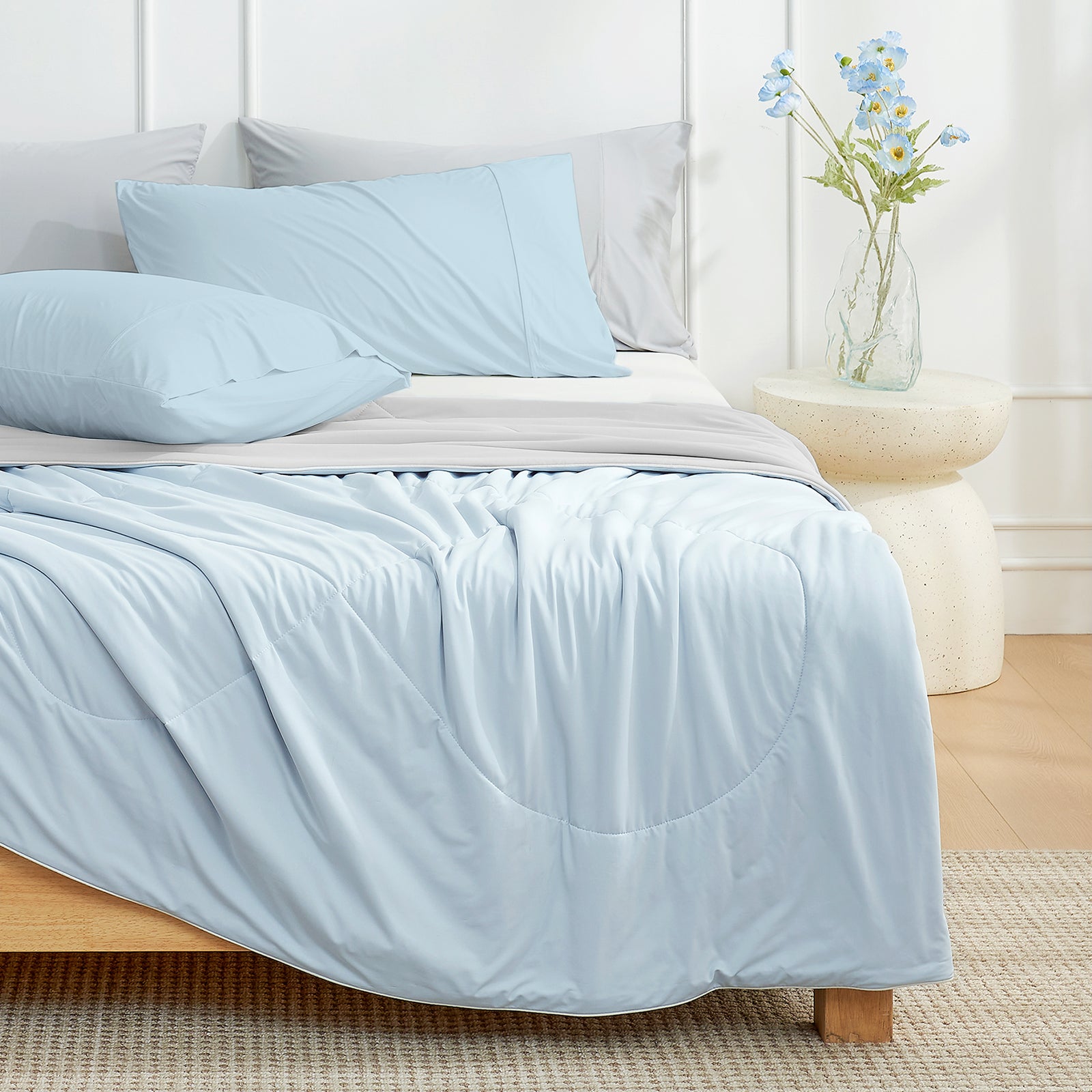 Snuggle Sac grey/blue Cooling comforter on a bed in a bedroom with a vase of flowers on a nightstand.#color_Grey/Blue