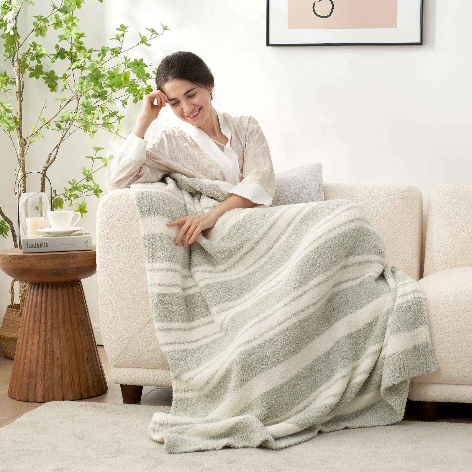 A woman wrapped in Striped Feather Yarn Knit Throw Blanket on a beige couch#Color_Sage Green